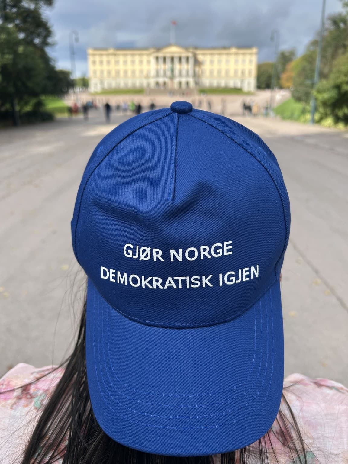 Person med blå PresseVern-caps foran Slottet i Oslo, med slagordet synlig.